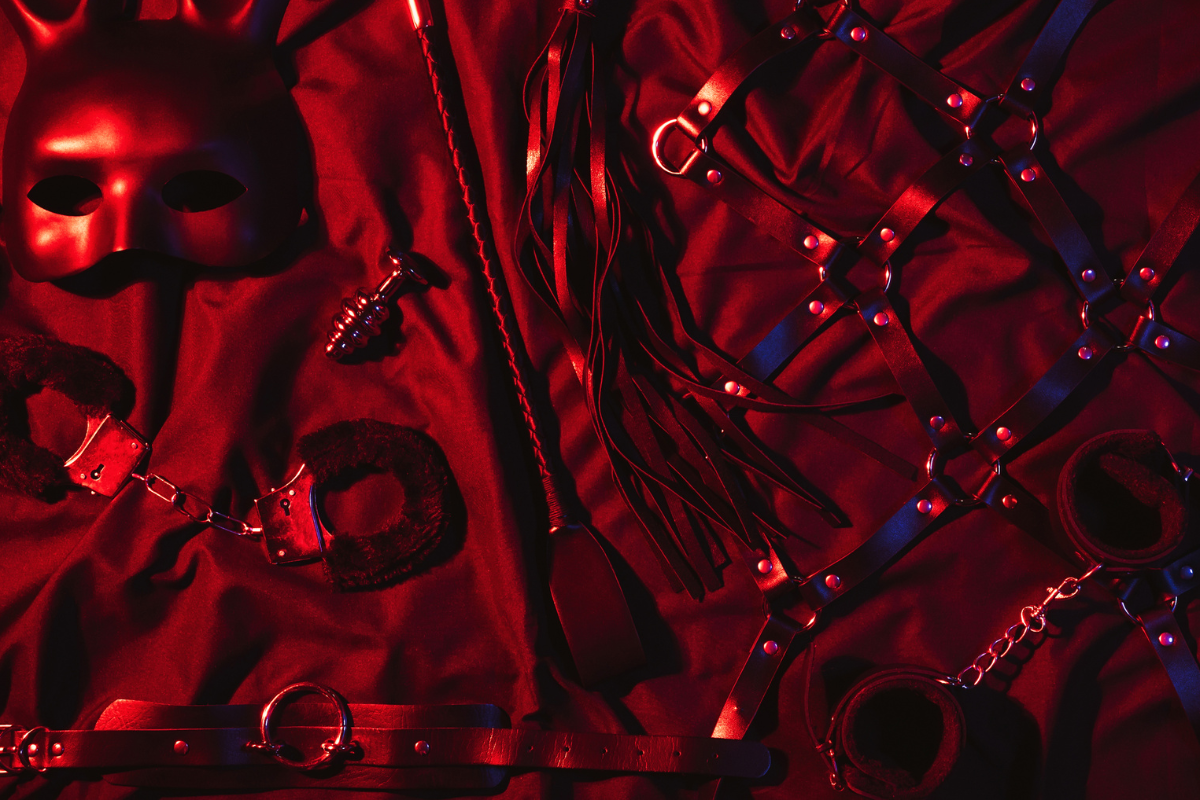 Akcesoria BDSM do karania &ndash; pejcz, packa i kajdanki na tle sypialni